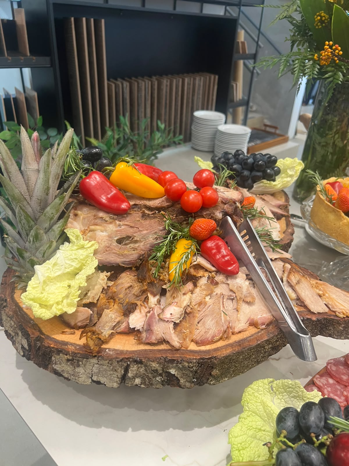 carne assada fatiada em prato de madeira rústica decorada com pimentões, tomilho, morangos e abacaxi, em um bu