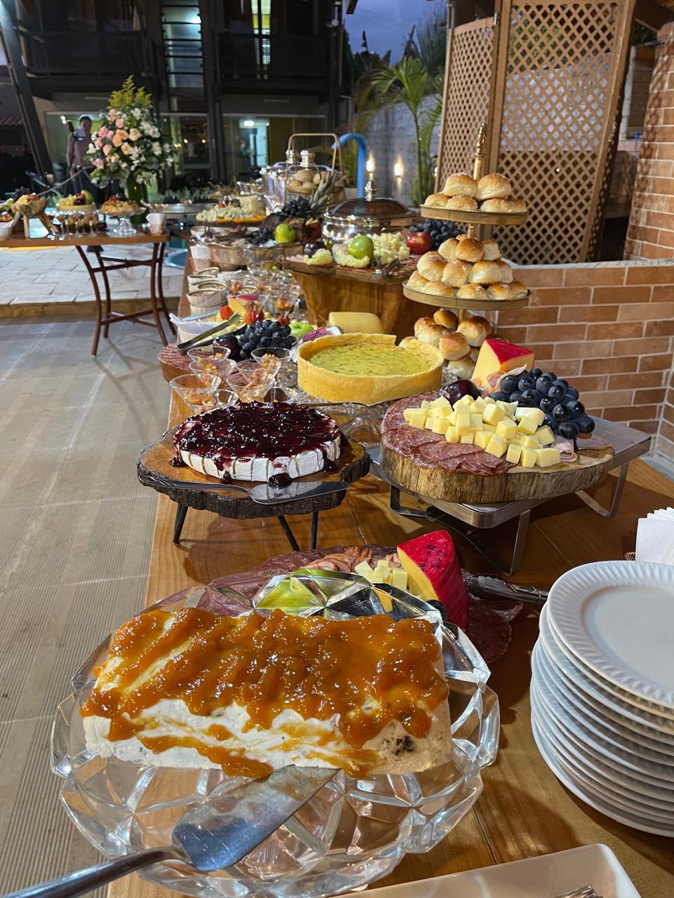 mesa de buffet de festas com tortas, queijes, frios, pães e frutas em travessas de vidro e madeira