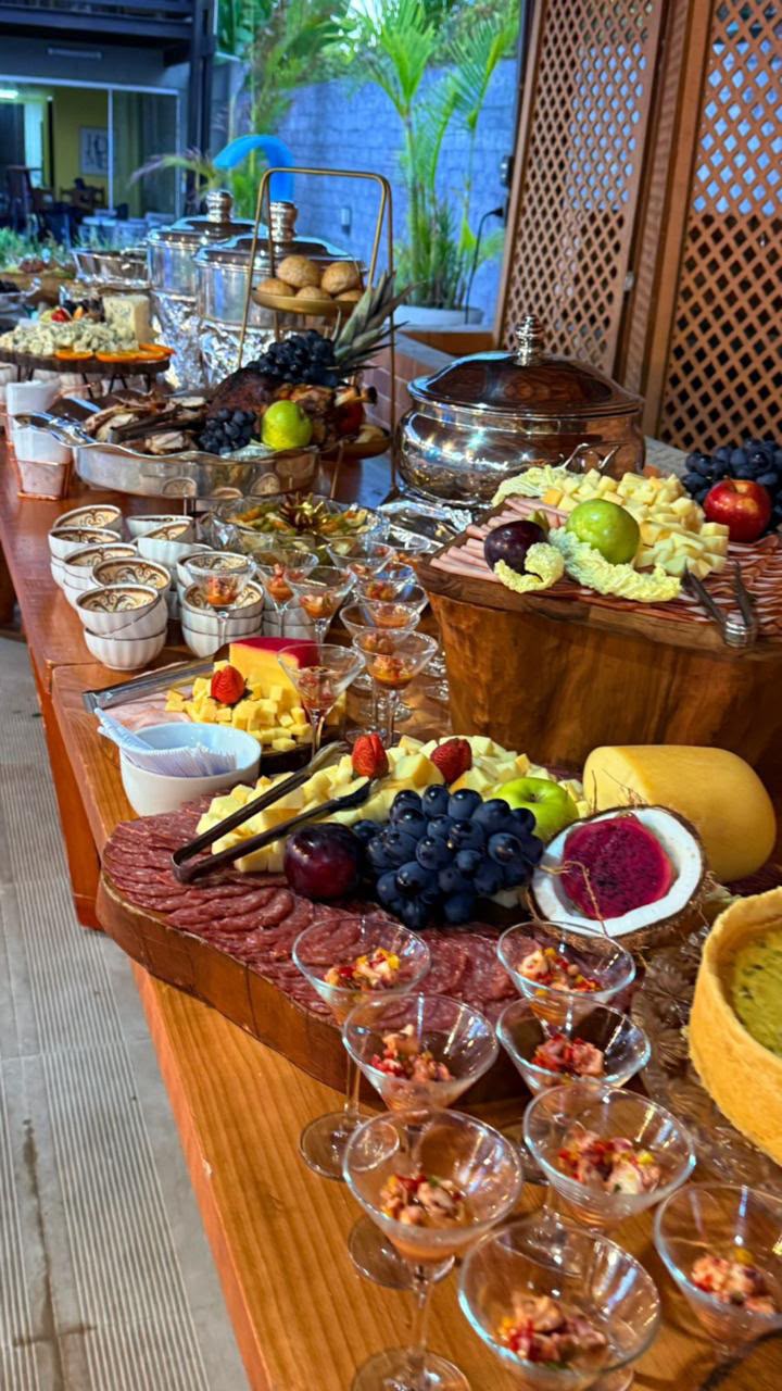 mesa de buffet de eventos com tábuas de frios, frutas, queijos, salgados em copinhos e rechauds de prata ao ar